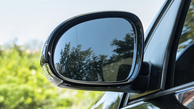 Close-up of a blank car side-view mirror reflecting trees and blue sky against a blurred green outdoor background. Automotive decal, sticker, or branding mockup.