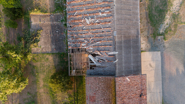 Aerial view of a damaged rural house roof with missing terracotta tiles and exposed wooden beams caused by a severe storm in Castelvetro Piacentino, Emilia-Romagna, Italy.