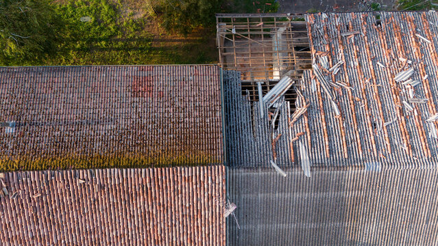 Aerial view of a rural house roof with storm damage, showing missing terracotta tiles and exposed rafters after a severe weather event in Castelvetro Piacentino, Emilia-Romagna, Italy.