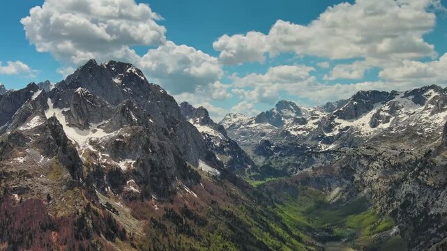 Aerial view of amazing rocky mountains in snow and green valley, Prokletie park, Montenegro and Albania, panorama 4k