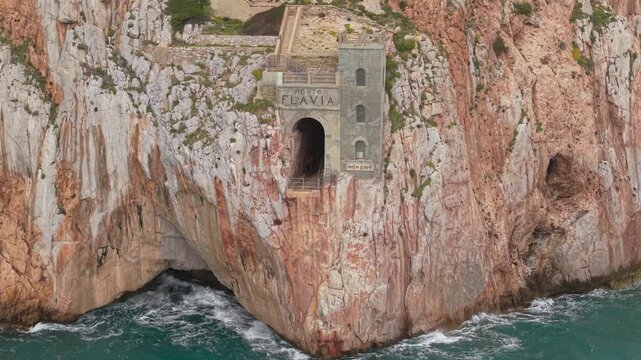 Porto Flavia Carved Into Steep Limestone Cliffs Of Masua Near Iglesias On The Southwest Coast Of Sardinia, Italy. Aerial Pullback Shot