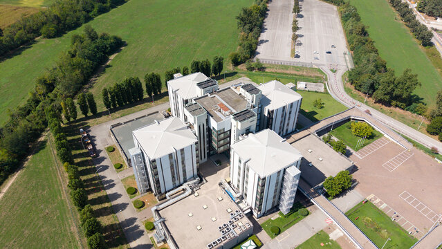 Aerial view of the STMicroelectronics semiconductor research and development facility featuring modern white buildings, surrounding parking lots, and green fields in Cornaredo, Lombardy, Italy.
