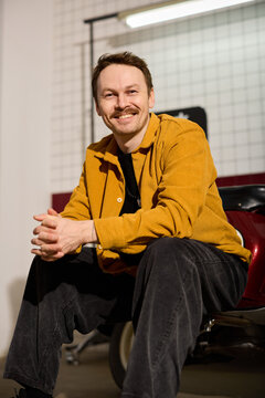 Pleasant male hairstylist positioned in traditional crimson salon armchair