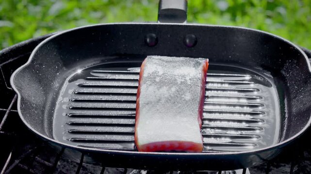 Closeup Of Cooking Salmon With Shimmering Oil And Green Landscape, Raw Pink Salmon Steak Sizzling On Grill With Glistening Oil And Lush Green Surroundings
