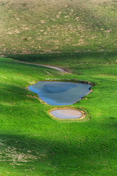 Aerial view of two small ponds nestled in a vibrant green grassy landscape with rolling hills in Italy.