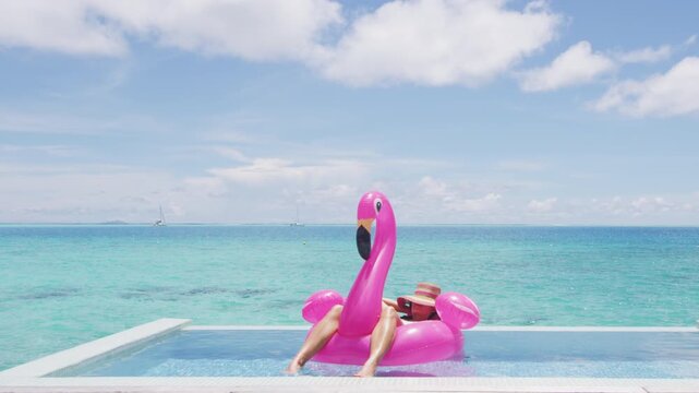 Travel vacation holidays concept. Woman in pool by beach sunbathing in bikini in inflatable pink flamingo toy mattress float in. Girl relaxing enjoying luxury lifestyle at resort pool.