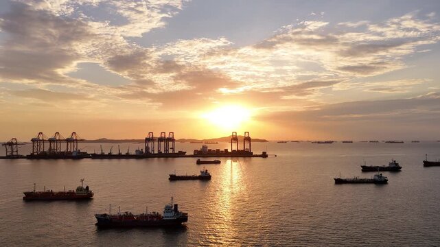 Silhouettes of gantry cranes and cargo ships at a bustling seaport during a dramatic golden sunset. Global maritime logistics, international trade, and industrial shipping transport concept.