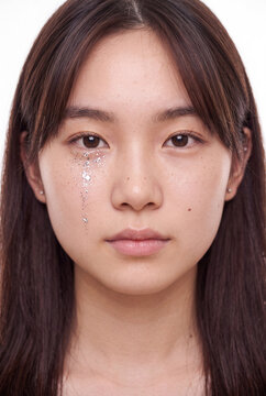 Frontal closeup portrait of a young woman with glitter tear detail for beauty background and cosmetics campaign design