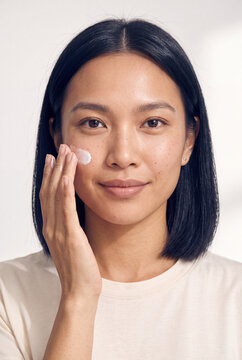 Young asian woman applying facial cream to cheek in natural light for skincare routine background and beauty banner
