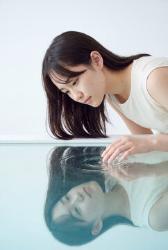 Young woman touching reflective water surface with contemplative expression for minimalist wellness background and calm poster design