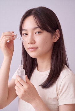 Young woman applying facial serum with dropper on clean background for skincare product banner and beauty design