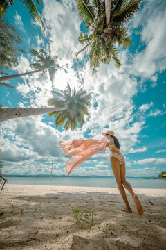 Woman tourist stay under shadow of the coconut trees at the edge of the sea beach, cheerfully traveling life in summer of the island
