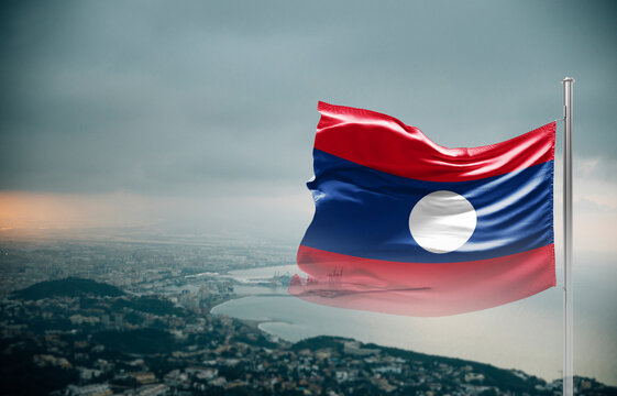 Laos flag waving over a coastal city under dramatic cloudy sky, realistic fabric motion, aerial seaside landscape background. Laos national flag for independence day.
