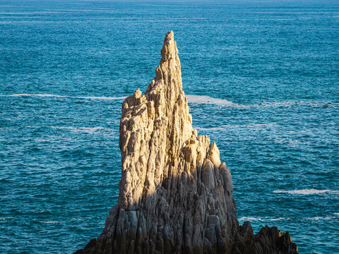 Aerial view of the Dedo de Dios rock formation rising from the deep blue waters of the Pacific Ocean with rugged textures and sunlight hitting the stone surface in Maruata, Michoacan, Mexico.