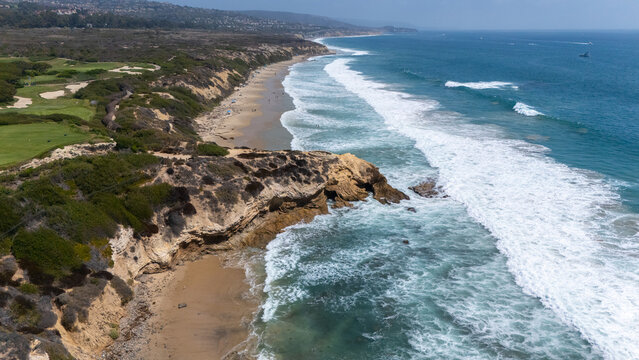 Aerial view of Crystal Cove featuring rugged cliffs, sandy beaches, and rolling waves along the Pacific coastline in Newport Beach, California, United States.