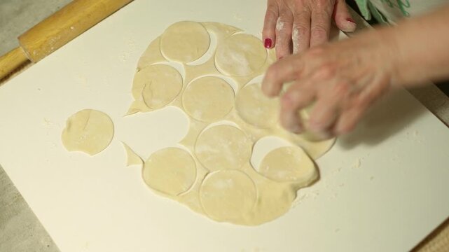 Woman hands rolling fresh dough for traditional pelmeni dumplings on flour dusted kitchen table, process of making homemade Russian food, authentic culinary cooking recipe preparation shot, 4K