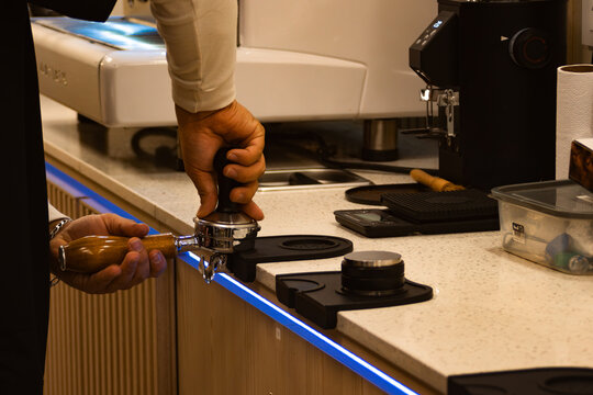 Barista preparing gourmet coffee, tamping fresh ground espresso beans into a portafilter, ensuring consistent extraction and rich aroma at a modern cafe