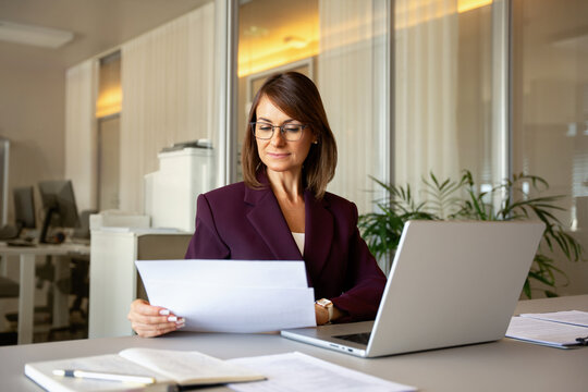 40s businesswoman reading document, reviewing paperwork at office desk. 40 years old business woman works as accountant analyst manager, filling official form, compiling annual statement. Copy space.