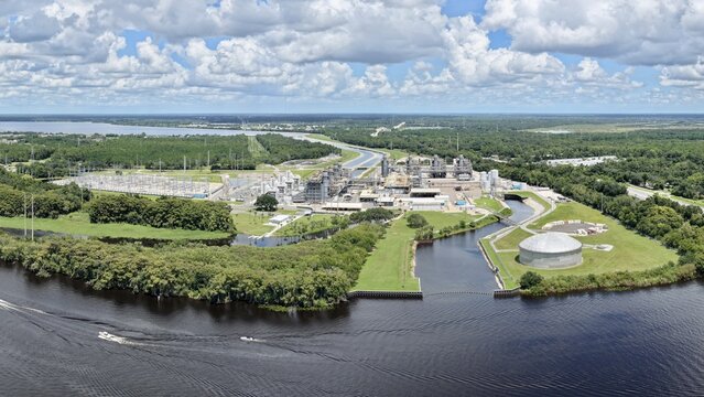Aerial view of the FPL Sanford Power Plant along the St. Johns River, featuring industrial infrastructure, storage tanks, and power lines amidst lush greenery in DeBary, Florida, United States.