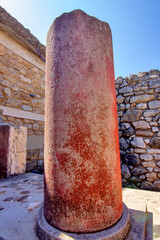Naklejka premium A close-up view of a red Minoan column standing among the ancient architectural remains of the Palace of Knossos on Crete, Greece.