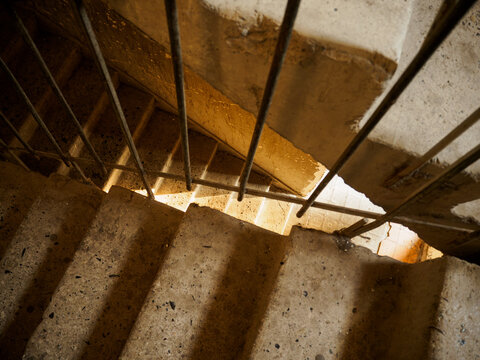 Horizontal top-down photo showing sunlight casting shadows on old concrete staircase steps behind a metal railing