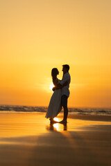 Fototapeta premium Couple stands on the beach at sunset with waves in the background and warm colors in the sky