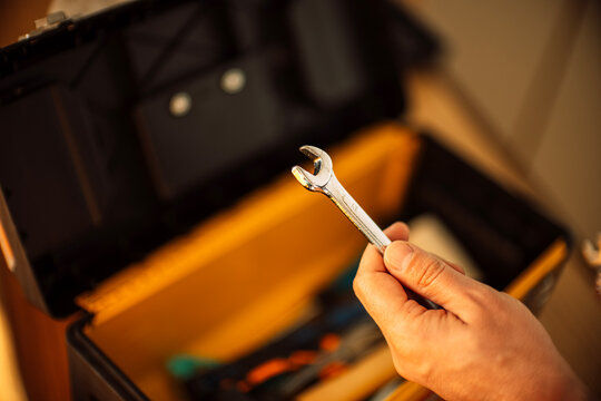 Hand holding a silver wrench above an open toolbox filled with various tools, showcasing a well-organized workspace for mechanical tasks and repairs