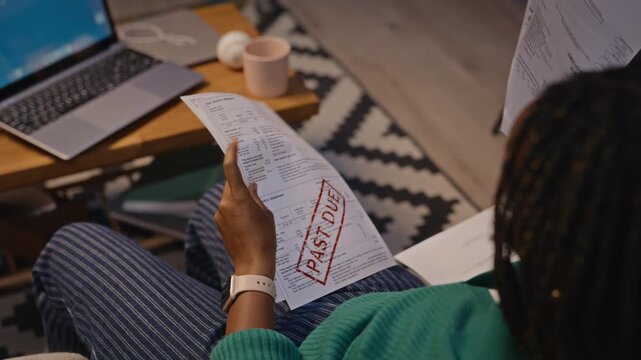 Young adult African American woman reviewing past due utility bills at home, managing personal finance. Footage is suitable for debt relief services or financial planning campaigns