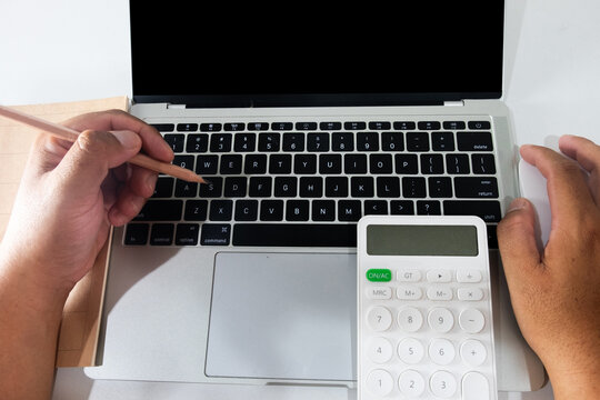 Top view of hands holding a pencil and mouse, working on a laptop with a blank screen and white calculator. Concept of accounting, budget planning, work from home, and financial data entry.