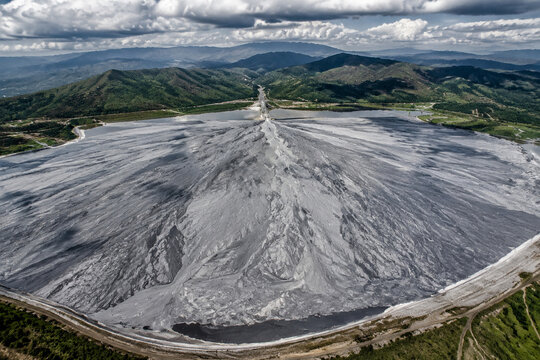A vast, fan-shaped field of grey mine tailings contrasting with distant green hills.