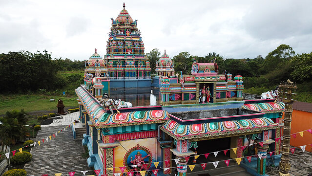 Aerial view of a colorful Hindu temple with an ornate gopuram, intricate statues, and festive bunting surrounded by lush greenery in Grand Gaube, Riviere du Rempart, Mauritius.