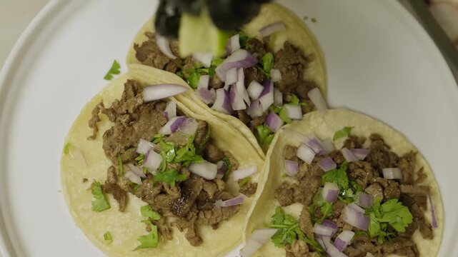 Chef squeezing fresh lime juice over authentic street tacos on white plate.