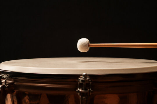 Drumstick poised just above the skin of a timpani drum.