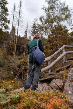 Hiker with backpack ascending a rustic wooden staircase in an autumn forest