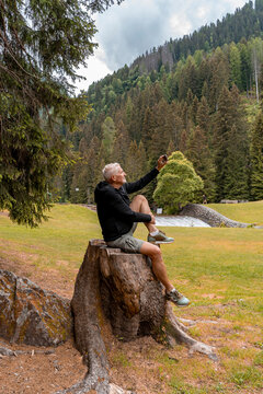 Senior man sitting on a tree stump in a park taking a selfie