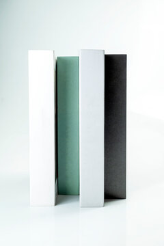 Four minimalist decorative books in white, mint green, grey, and black standing vertically on a clean white background. Study or education concept