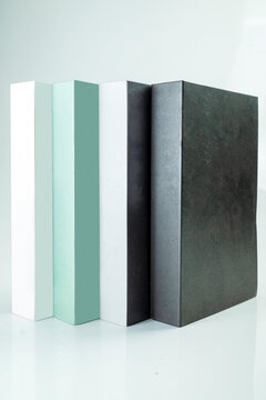 Four minimalist decorative books in white, mint green, grey, and black standing vertically on a clean white background. Study or education concept