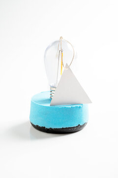 Minimalist light blue and black round dessert topped with a clear light bulb and a triangular tag, isolated on a white background. Mockup or Copyspace