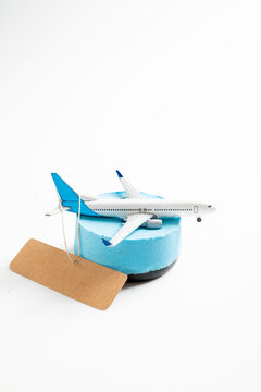 Model airplane on a blue stand with a blank brown luggage tag against a white background, representing travel, tourism, and flight bookings. Mockup or Copyspace