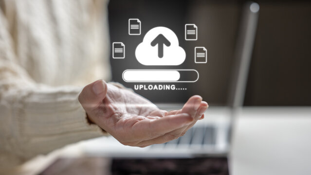 Female hand holding a holographic cloud upload icon with file symbols and a progress bar above a laptop. Concept of cloud computing storage and digital storage technology