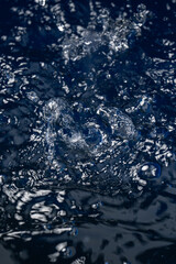 Water splash and dynamic ripples on dark blue liquid surface. High speed action shot of water droplets. © Komkrit