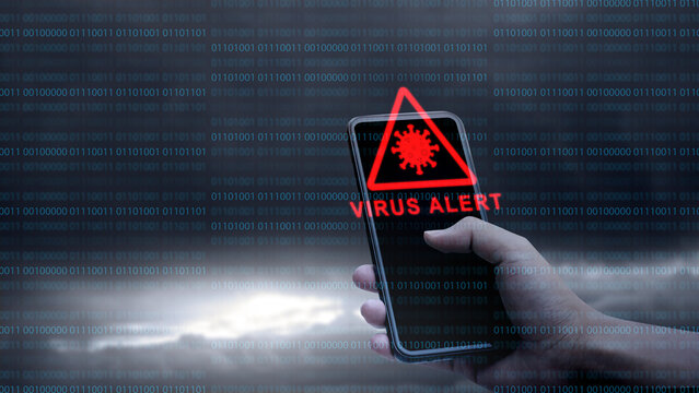 A hand holding a smartphone showing a red 'VIRUS ALERT' warning icon, set against a dark background with digital binary code. Concept of Technology Security