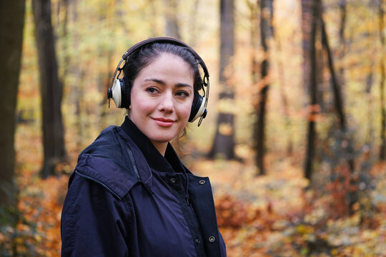 Relaxed young woman wearing headphones and enjoying music on autumn walk through forest