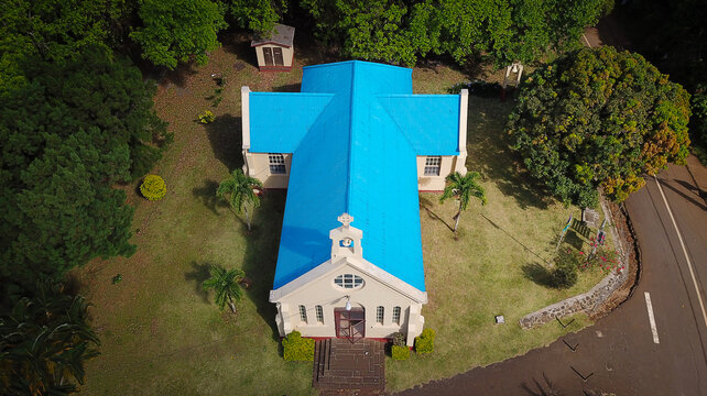 Aerial view of Chamarel Church with its bright blue roof, surrounded by lush trees and lawns in a peaceful setting Chamarel, Riviere Noire District, Mauritius.