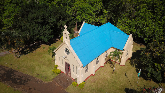 Aerial view of the historic Chamarel Church featuring a distinctive bright blue roof, surrounded by lush green trees and manicured lawns in Chamarel, Riviere Noire District, Mauritius.