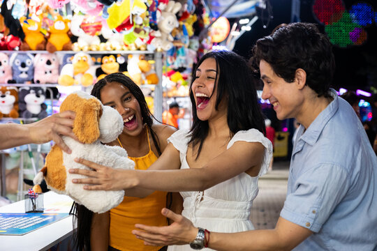 Excited friends receiving a stuffed animal prize at a bustling night fair