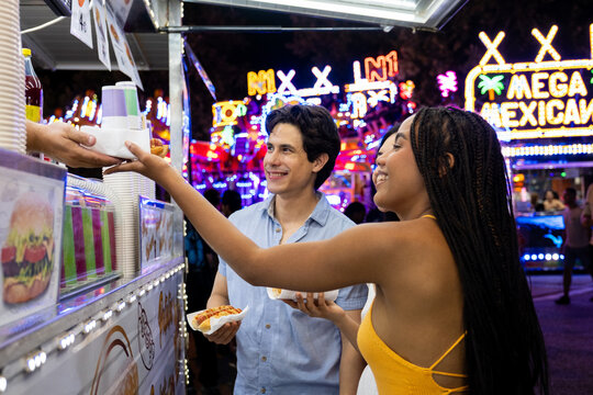 Happy couple receiving hot dogs and drinks from a food truck vendor at a vibrant night fair