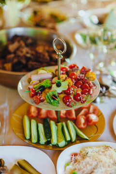 Photo of food, fresh vegetables, tomatoes, meat, canapes with olives on a two-tiered plate on a table in a restaurant.