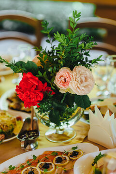 Photo of a beautiful fresh bouquet of roses on a decorated table with food in a restaurant.