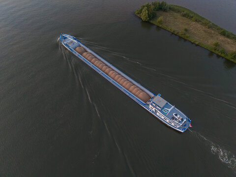 Aerial view of a large inland cargo ship carrying bulk material along a river in The Netherlands.